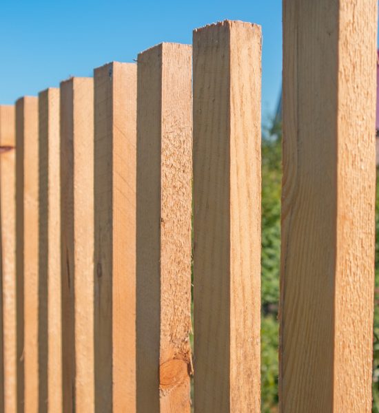 Close-up of a new wooden picket fence in the backyard of a country house, a sunny summer day